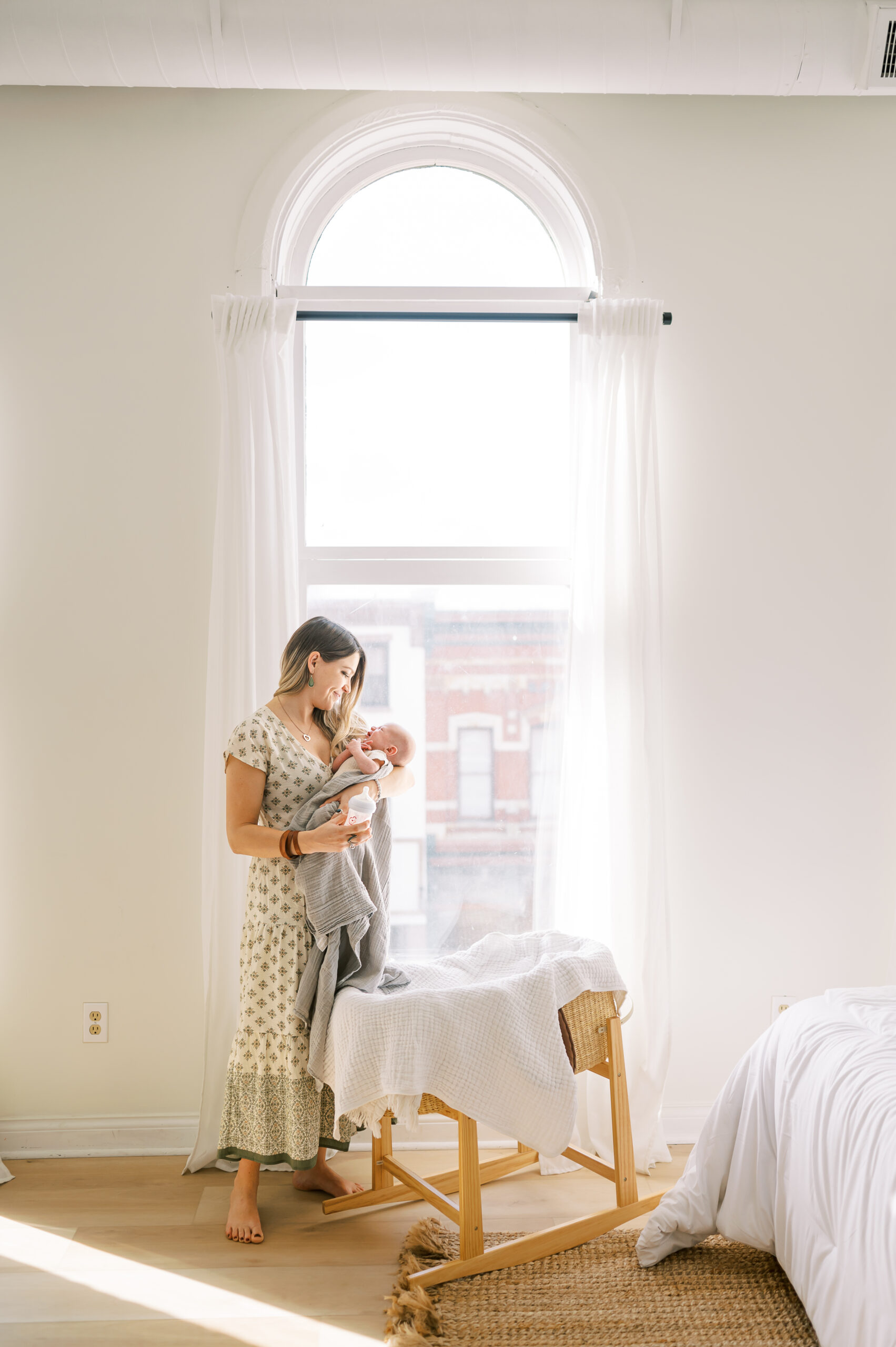 Mom standing in front of tall window holding newborn baby